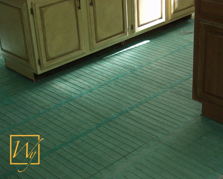 TempZone electric radiant floor heating mesh with blue heating cables installed on a kitchen subfloor between base cabinets.