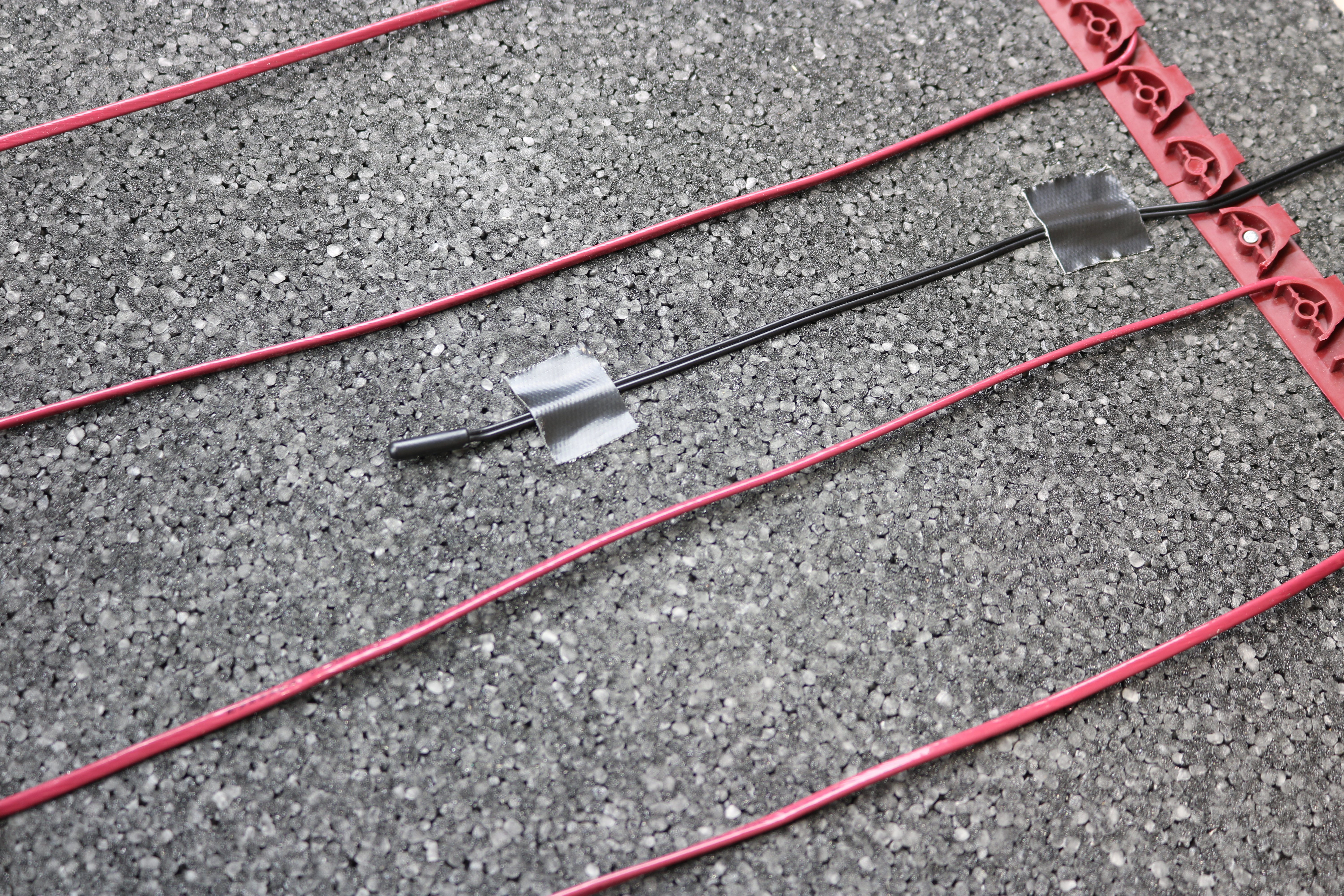 TempZone electric radiant floor heating cable installed on foam underlayment with a floor sensor probe and red plastic fixing strips.