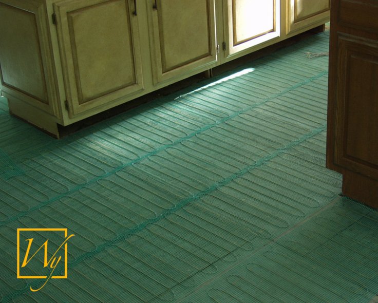 TempZone electric radiant floor heating mesh with blue heating cables on green fiberglass matting installed on a kitchen subfloor.