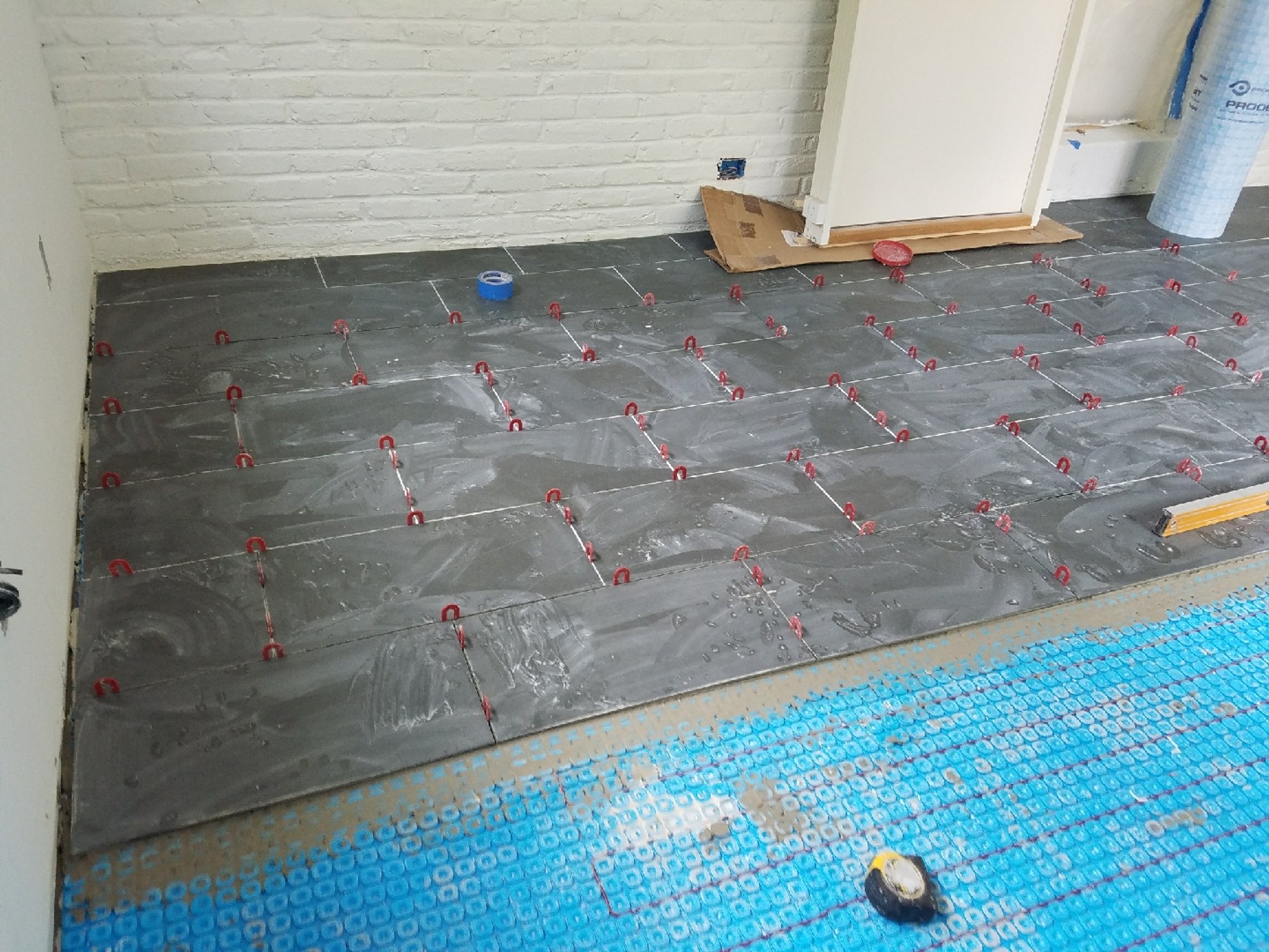 Tile floor being installed over Prodeso uncoupling membrane with electric floor heating cable