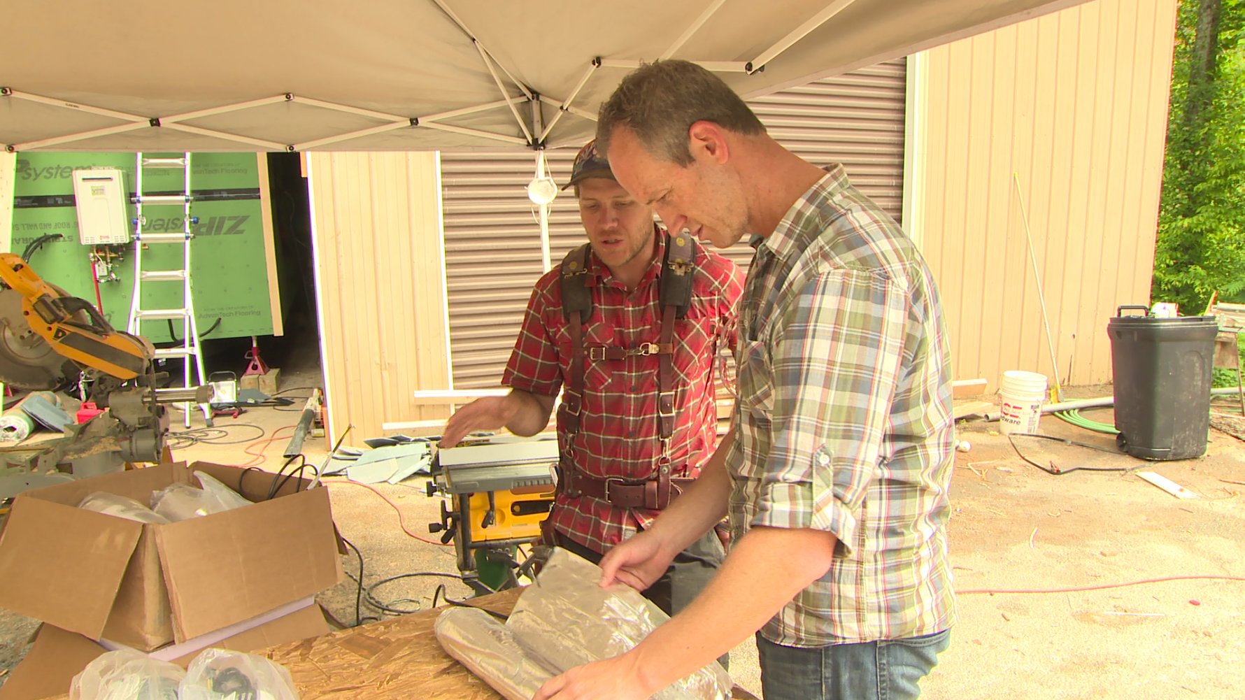 Zack Giffin and a colleague examining packaged Environ Flex Rolls electric radiant floor heating mats on a plywood work surface.