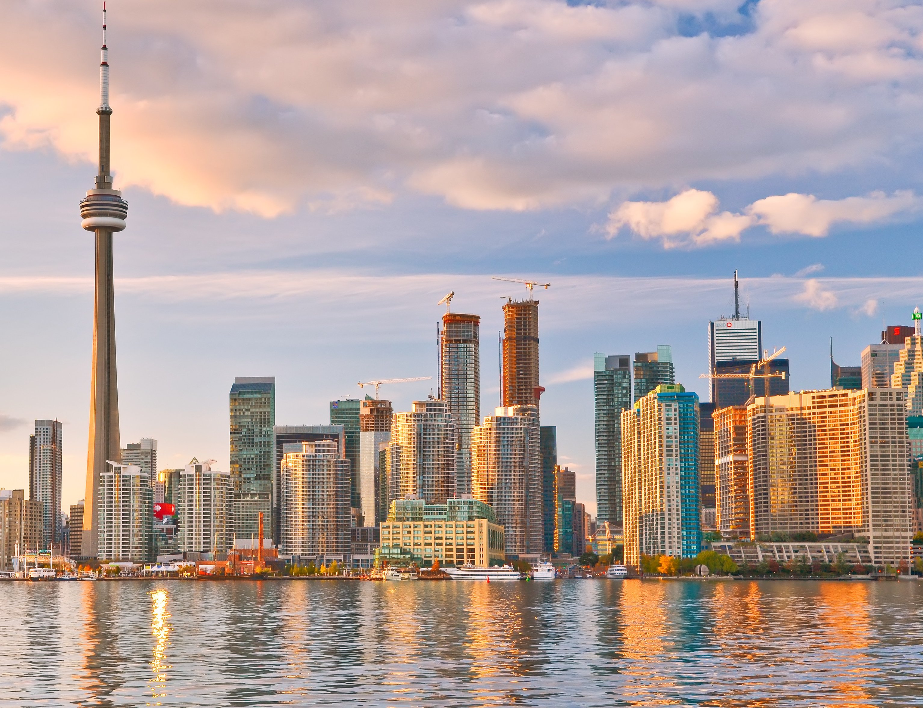 The Toronto city skyline featuring the CN Tower and waterfront skyscrapers illuminated by a golden sunset.