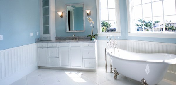 A traditional bathroom with white tile flooring, a freestanding clawfoot bathtub, and a white vanity with a marble countertop.