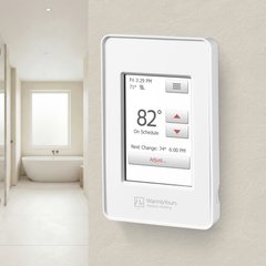 A WarmlyYours nSpire Touch programmable thermostat mounted on a wall to control an electric radiant floor heating system in a modern bathroom.