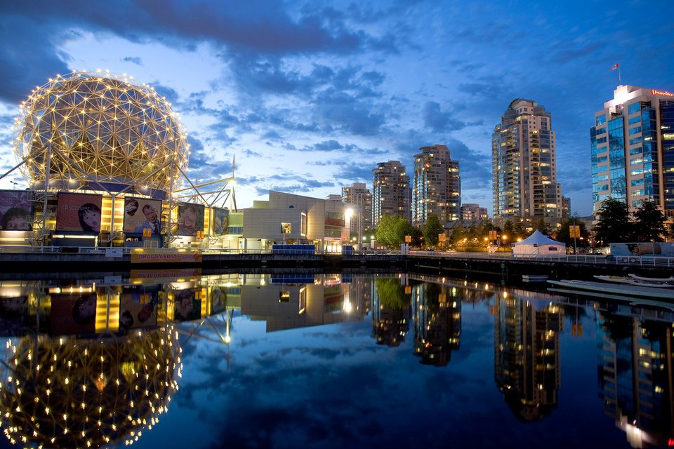 The Vancouver skyline at dusk featuring the illuminated Science World dome and waterfront high-rises reflecting in False Creek.