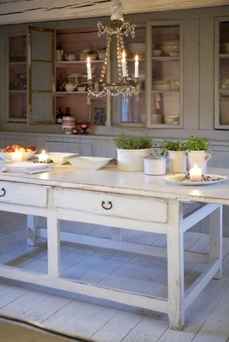 A rustic cottage dining area with a distressed white wooden table and lit candles, featuring an electric radiant floor heating system.