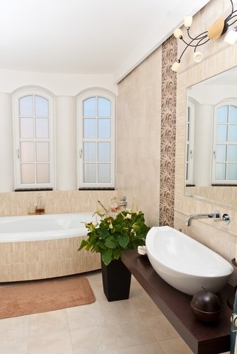 A modern bathroom featuring a neutral tiled floor, a curved drop-in bathtub, and a floating vanity with a white vessel sink.