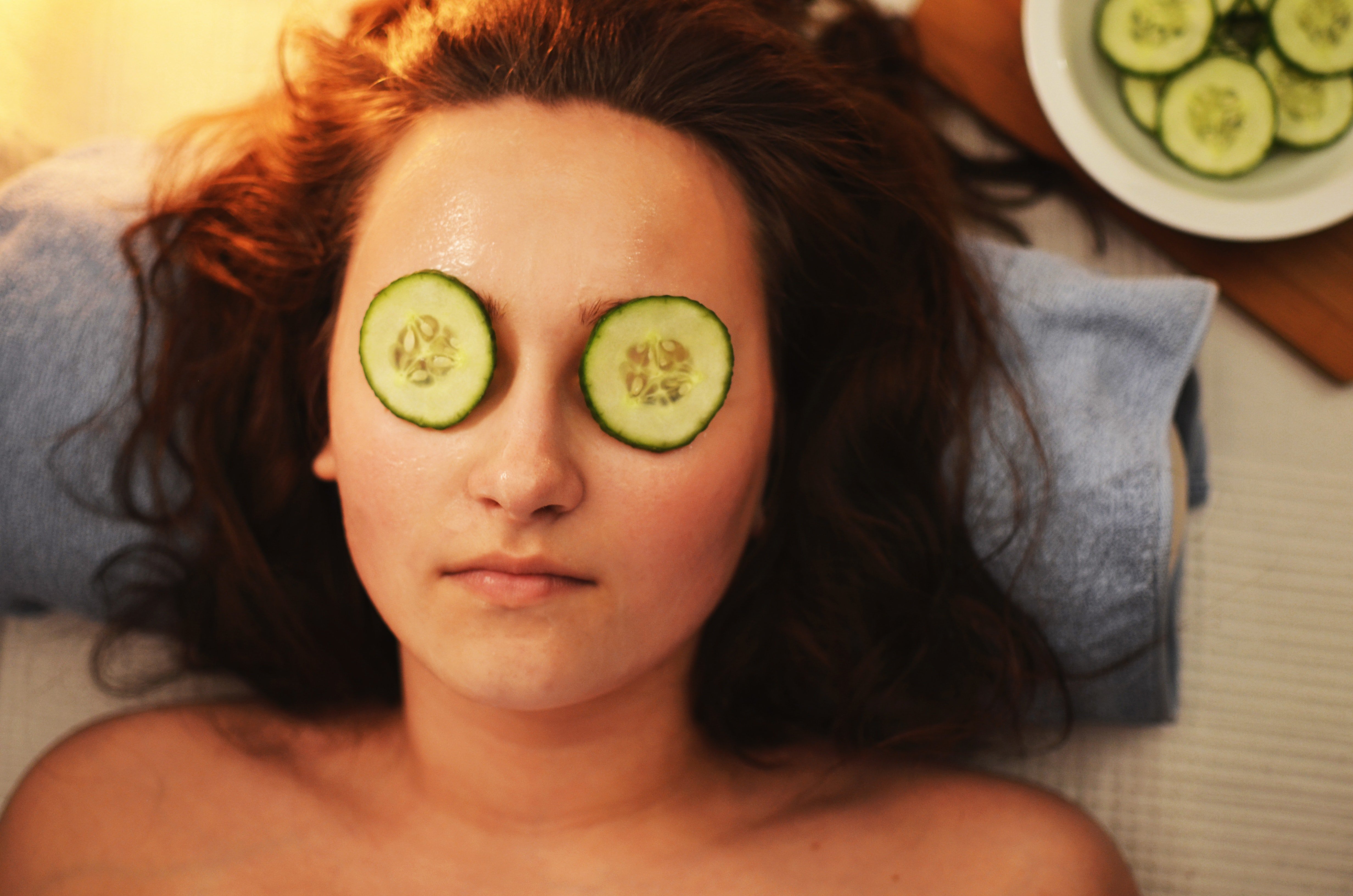 A woman relaxing during a spa treatment with cucumber slices on her eyes while resting her head on a blue towel.