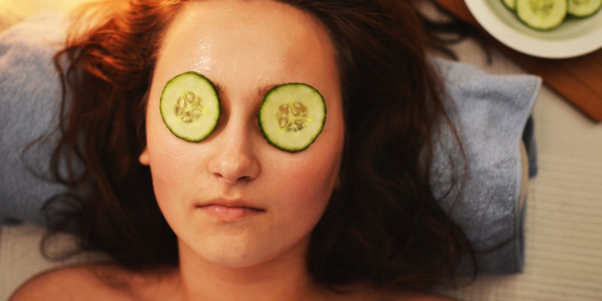 A woman relaxing during a spa treatment with cucumber slices on her eyes while resting her head on a blue towel.