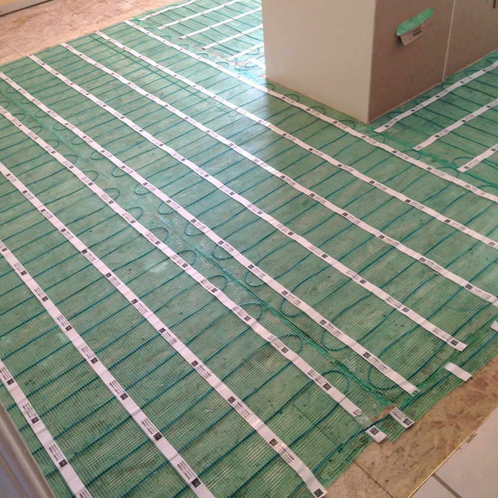 Electric floor warming roll installed for full coverage heating above a wood subfloor