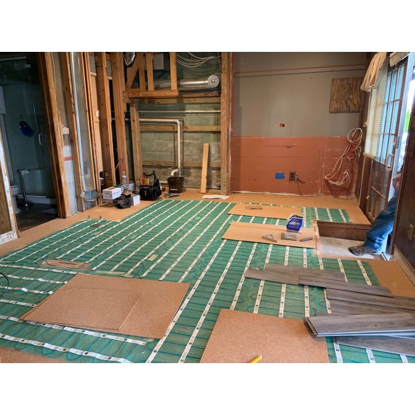 Electric floor heating rolls being installed with cork underlayment in basement remodel